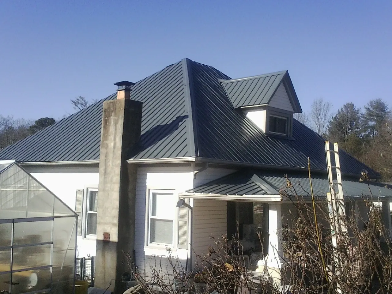 Dark blue standing seam metal roof on a white farmhouse with dormer — Slate & Tile Roof Repair by Roofing Brothers in Dornsife