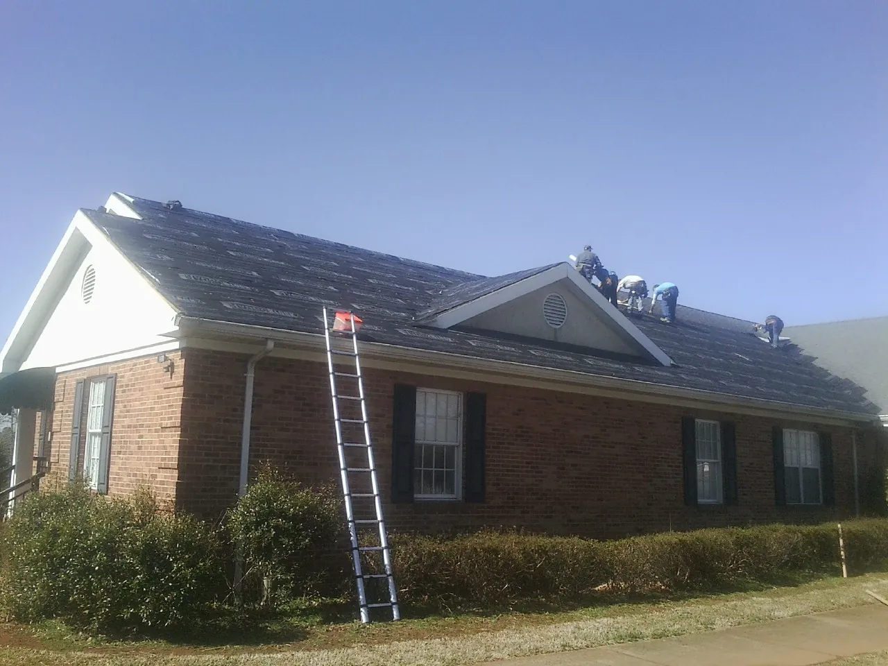 Crew tearing shingles off a brick ranch roof with a ladder set — Emergency Roof Repair work by our crew in Dornsife