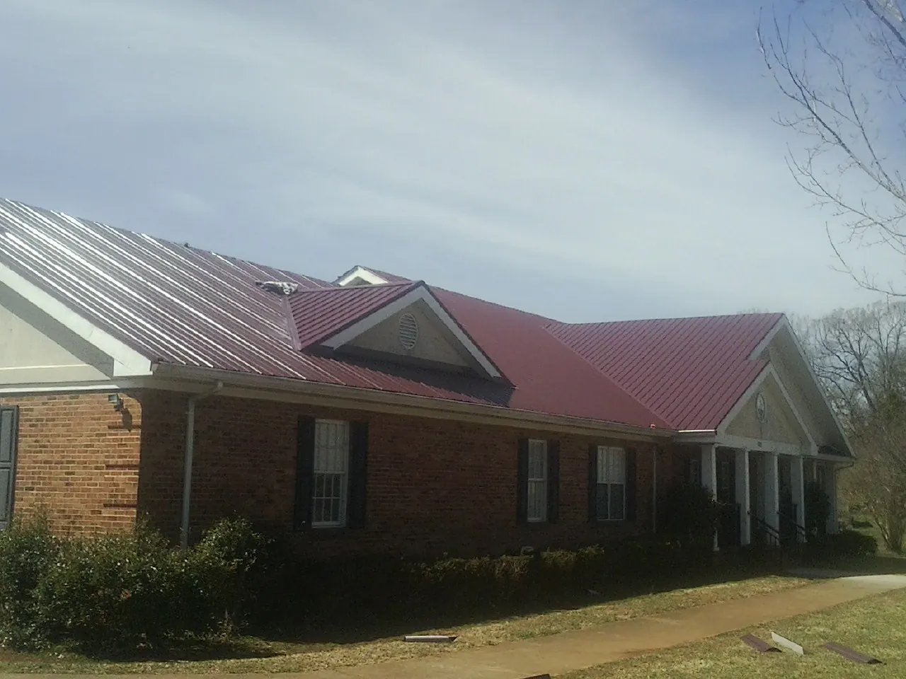 Red metal roof with gabled entries on a long brick building, from a Hail Damage Roof Repair job in Dornsife