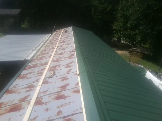 Old rusted panels beside newly installed green metal roofing — Wind Damage Roof Repair by Roofing Brothers in Dornsife