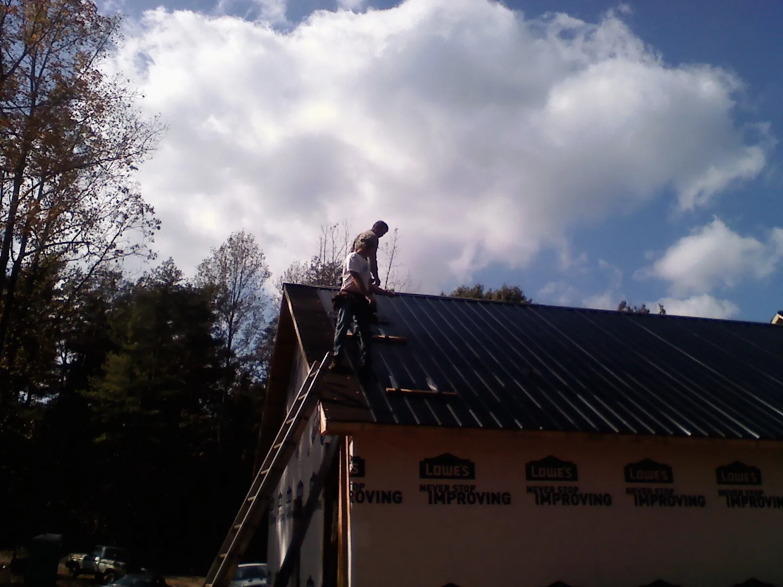 Roofer fastening dark metal panels high against a cloudy sky, from a Roof Inspection job in Dornsife