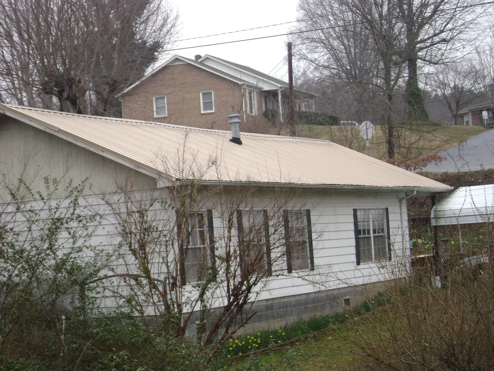 Tan metal roof on a white sided house set into a hillside — Commercial Roofing by Roofing Brothers in Dornsife